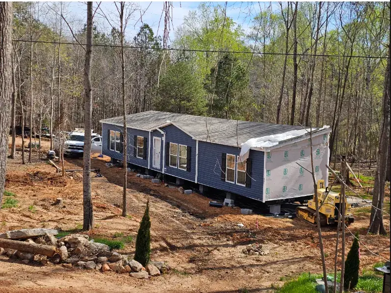 Blue mobile home being set on its piers with a dozer beside it