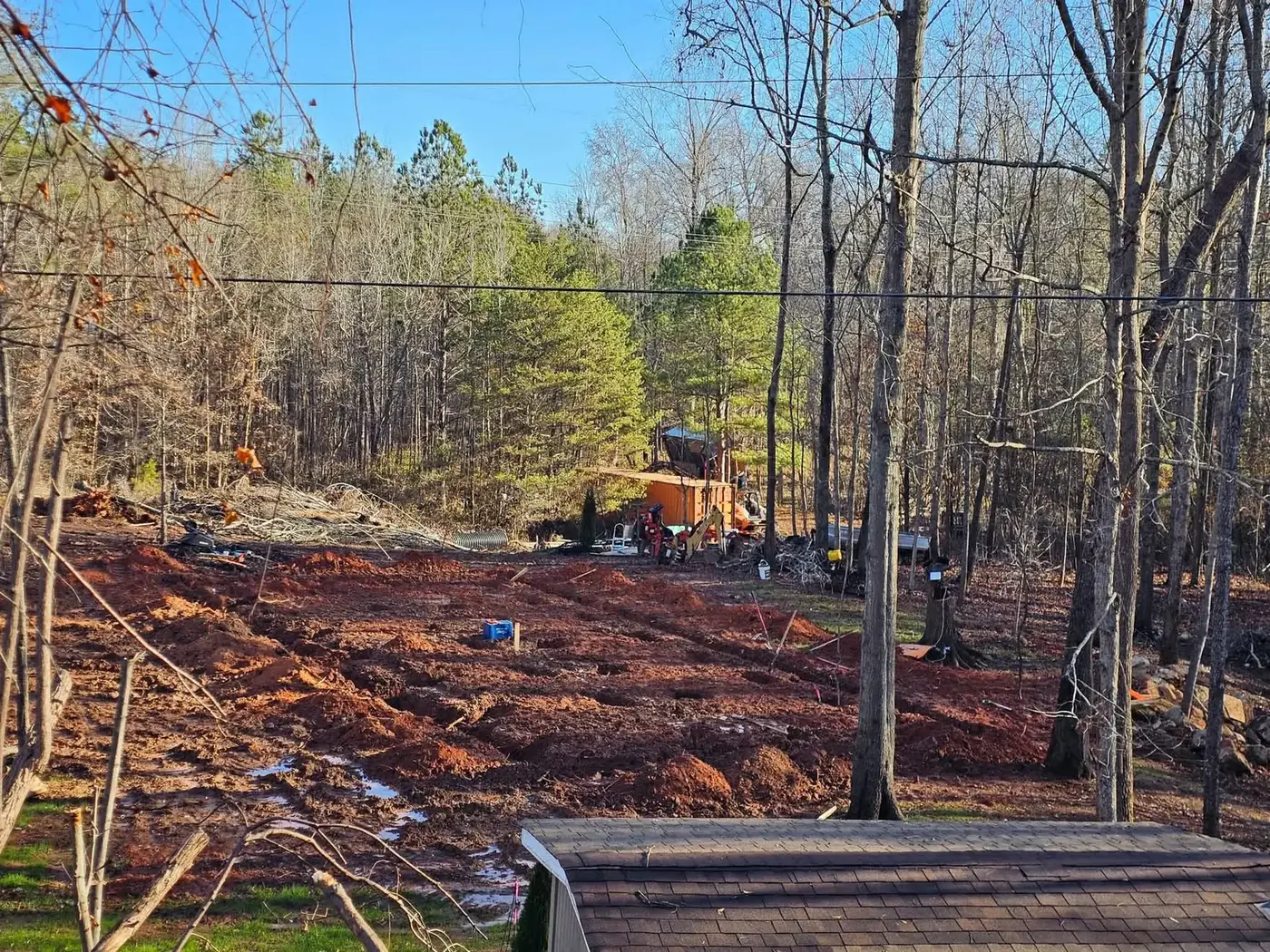 Cleared red clay site with footer locations marked and equipment in the background