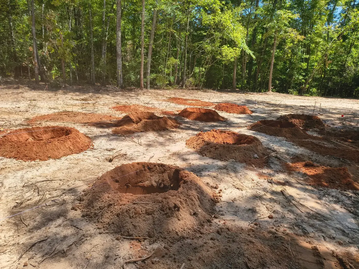 Footer holes dug in a grid with string lines and piles of red clay