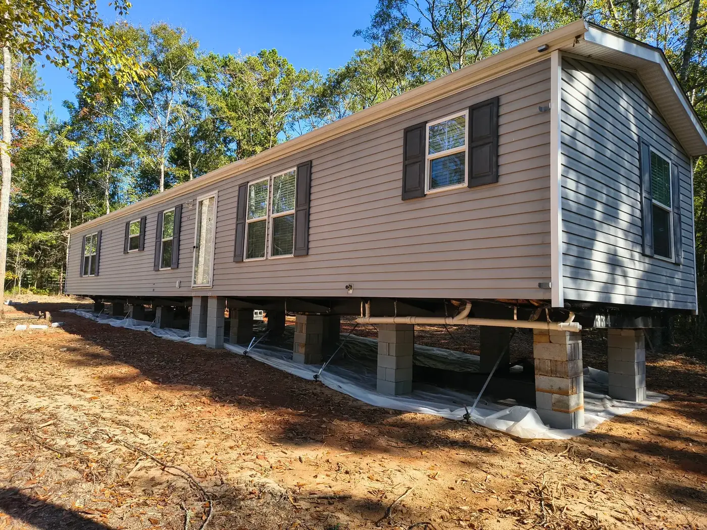 Side view of a gray mobile home with dark shutters set on block piers